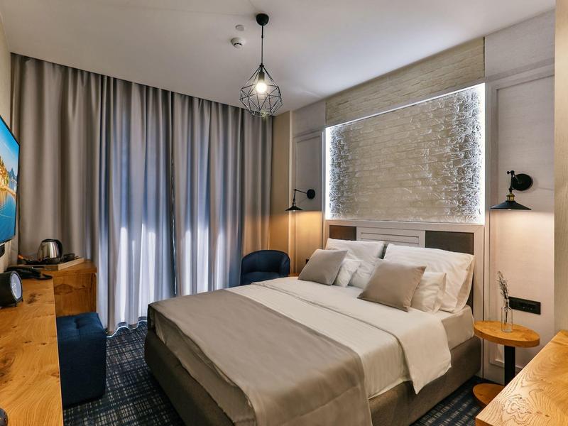 Modernes Schlafzimmer mit großem Bett, grauen Vorhängen und Holzmöbeln in neutralen Farben.