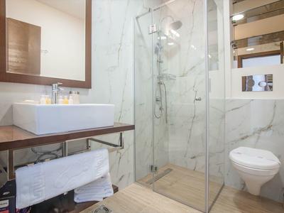 Modernes Badezimmer mit Eckdusche, weißem Waschbecken, Holzregal und wandhängendem WC.