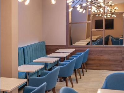 Modernes Café mit blauen Stühlen, weißen Tischen und auffälligen Deckenlampen in warmem Licht.