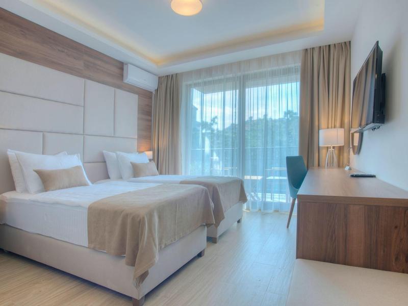 Hell eingerichtetes Hotelzimmer mit zwei Einzelbetten, großem Fenster und modernem Holzmobiliar.