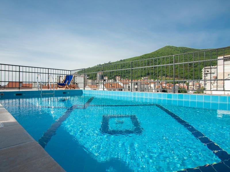 Blauer Pool mit klaren Wasser, Umzäunung und Berg im Hintergrund unter blauem Himmel.