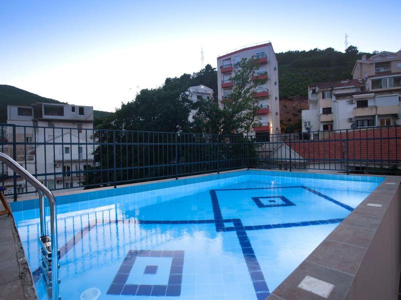 Freier Pool auf Dachterrasse mit Metallgeländer und umliegenden Gebäuden bei Dämmerung.