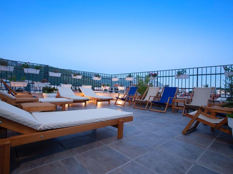 Dachterrasse mit mehreren Holzloungemöbeln, blauer Himmel und Metallgeländer im Hintergrund.