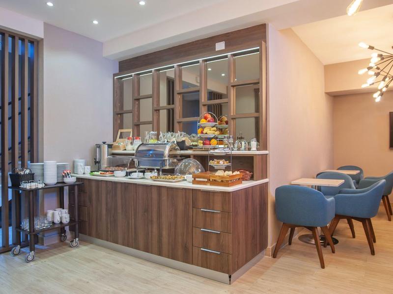 Moderner Frühstücksbereich mit Holztheke, blau gepolsterten Stühlen und stilvollen Leuchten.