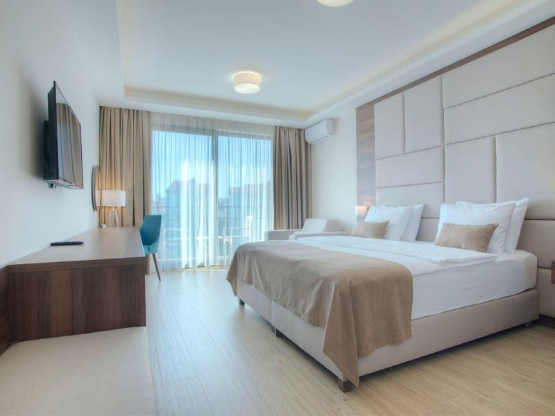 Modernes Schlafzimmer mit Doppelbett, Fernsehgerät, Schreibtisch und großen Fenstern mit Vorhängen.