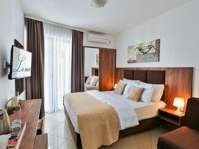 Camera d'hotel moderna con letto matrimoniale, lampade da comodino e finestra con balcone e tende.