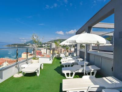 Terrazza sul tetto con lettini e ombrelloni con vista sul mare sotto un cielo sereno.