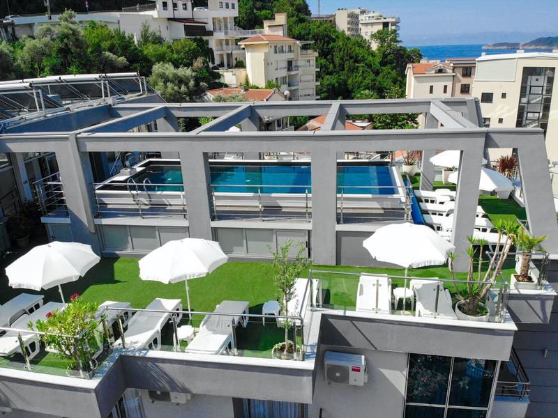 Moderne Dachterrasse mit grünem Rasen, weißen Sonnenschirmen und Swimmingpool bei Tageslicht.