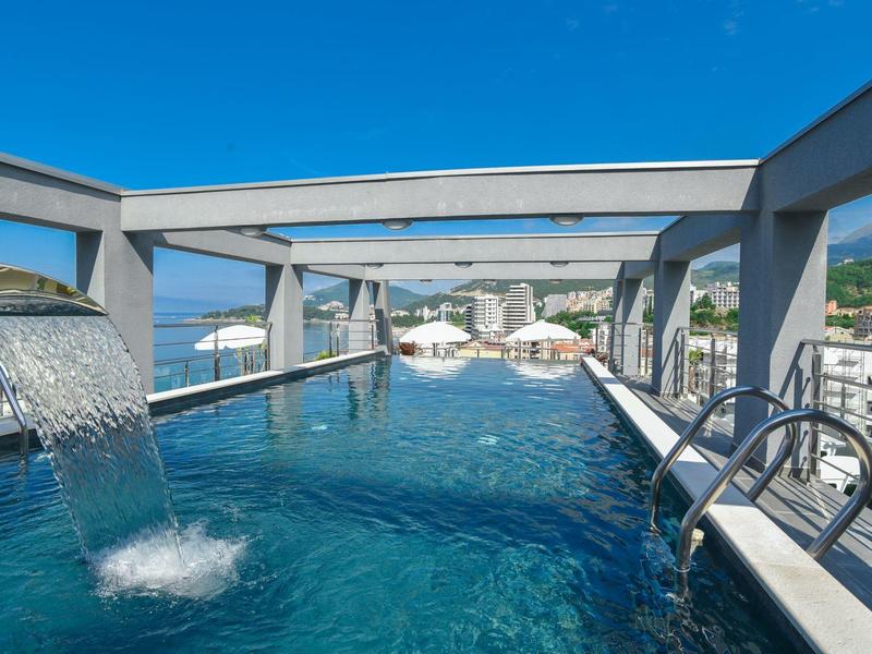 Moderner Infinity-Pool mit Wasserelement, metallischen Geländern und blauem Himmel im Hintergrund.