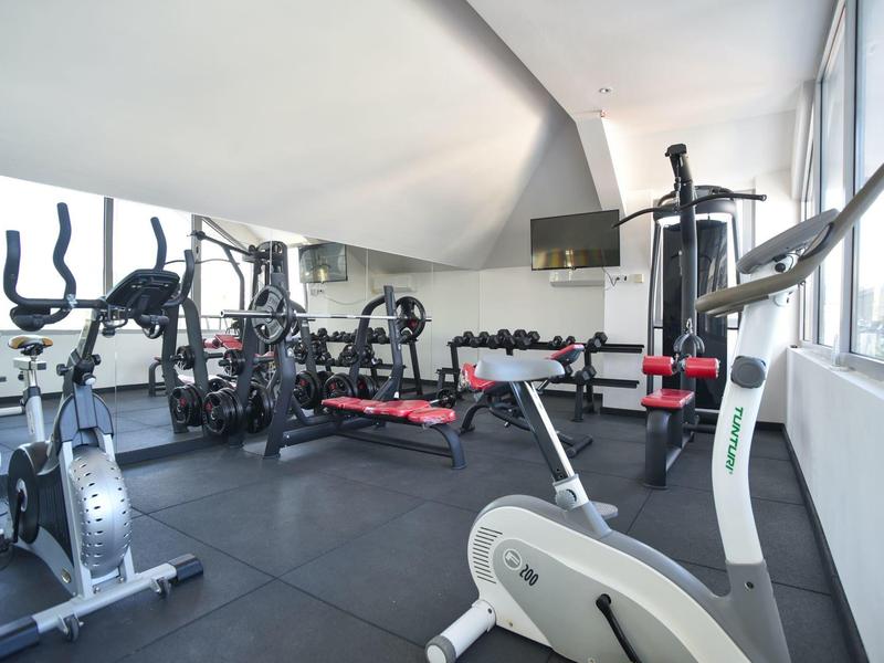 Helles Fitnessstudio mit modernen Geräten, Gewichten, Spiegelwand und großen Fenstern.