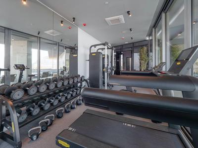 Palestra moderna con tapis roulant, pesi e macchine per allenamento vicino a grandi finestre.