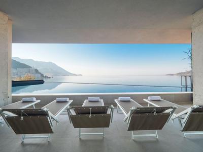 Lettini moderni su una terrazza con piscina a sfioro e vista sul mare e sulle montagne.