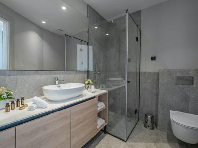 Modernes Badezimmer mit Glasdusche, weißem Waschbecken und Holzunterschrank, grauen Fliesen und WC.