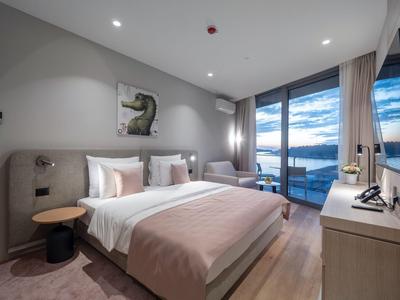 Camera d'hotel moderna con letto matrimoniale, poltrona, grande finestra con vista sul lago e arredamento minimalista