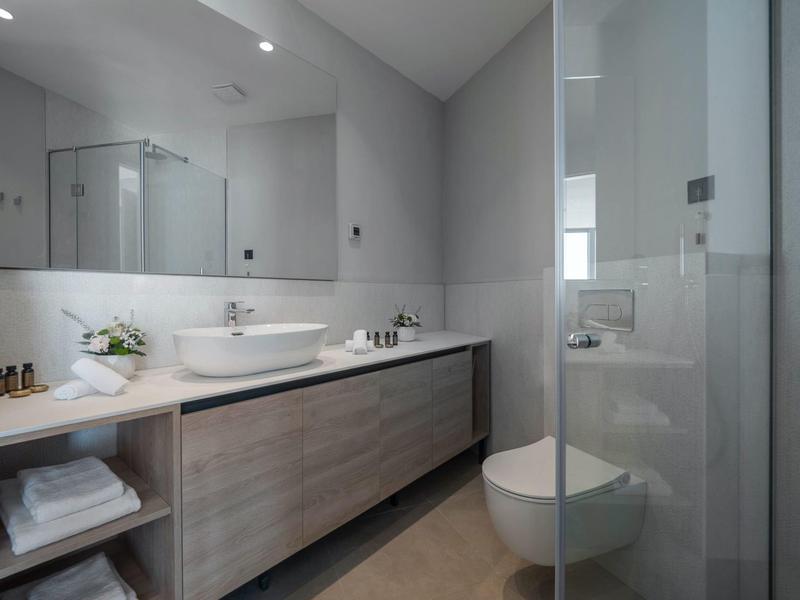 Moderne hellgraue Badezimmer mit großem Spiegel, Waschtisch mit Holzschrank und Glas-Duschabtrennung.