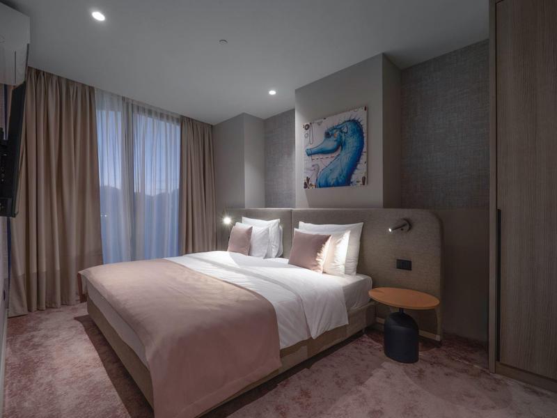 Modernes Schlafzimmer mit großem Bett, brauner Bettdecke, grauen Wänden und gemaltem Wellenbild.