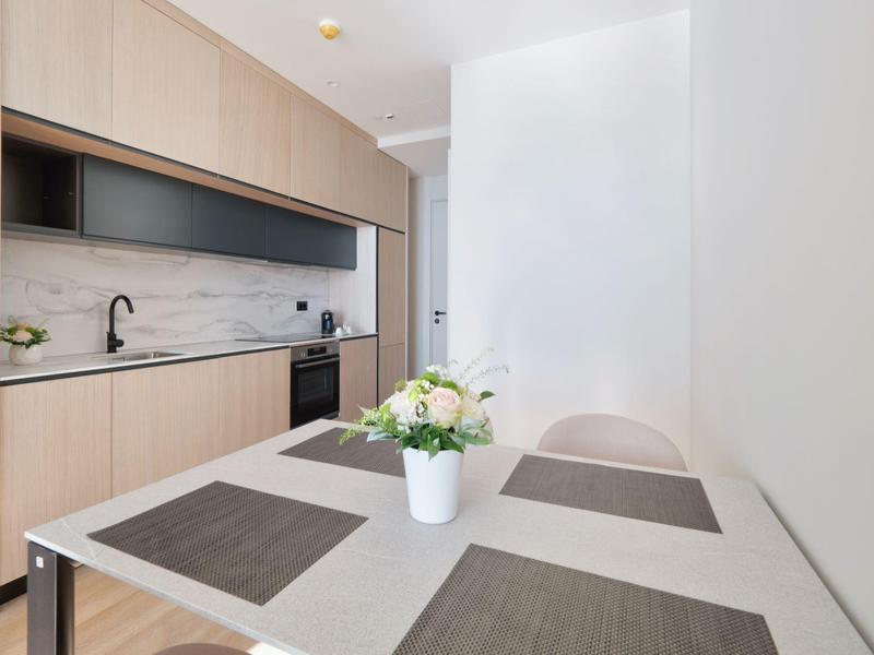 Moderner Küchenbereich mit hellem Holz, schwarzem Wasserhahn und weißem Esstisch mit Blumenarrangement.