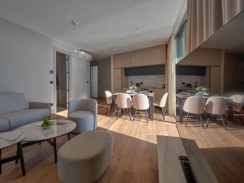 Helles Wohnzimmer mit grauem Sofa, ovalem Couchtisch und offenem Essbereich mit sechs Stühlen.