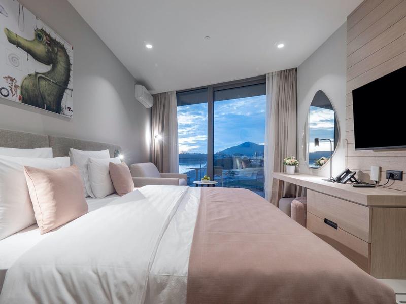 Modernes Schlafzimmer mit großem Bett, rosa Decke, Fenster mit Bergblick und TV an der Wand.