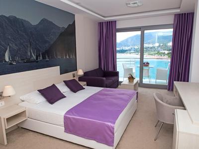 Camera d'hotel moderna con letto matrimoniale, accenti viola e balcone con vista mare.