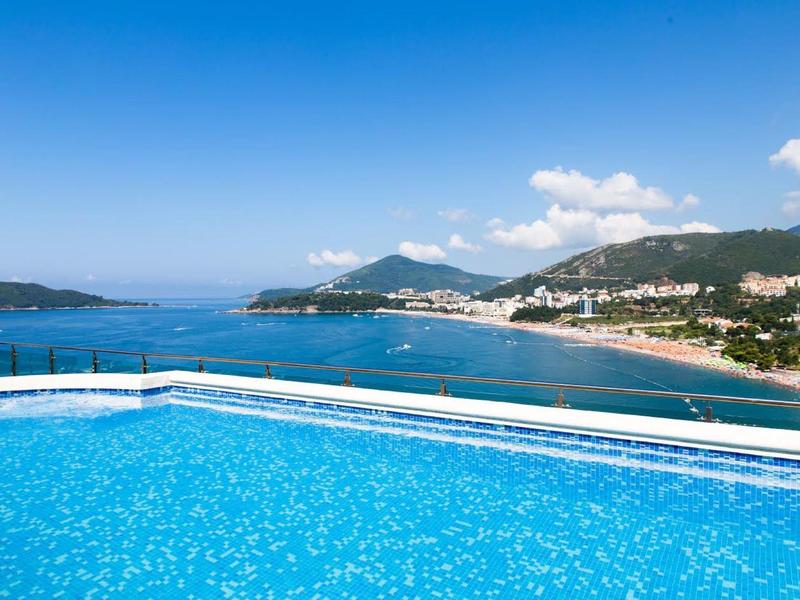 Ein blauer Swimmingpool mit Meerblick und Bergen unter blauem Himmel mit wenigen Wolken.