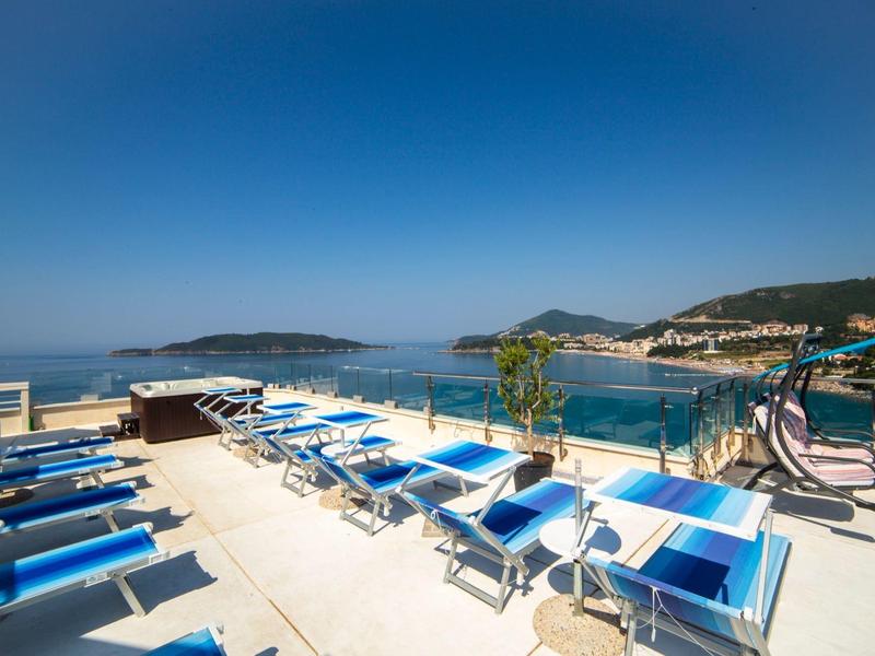 Dachterrasse mit blauen Liegestühlen, Meerblick und klarem Himmel am sonnigen Tag.