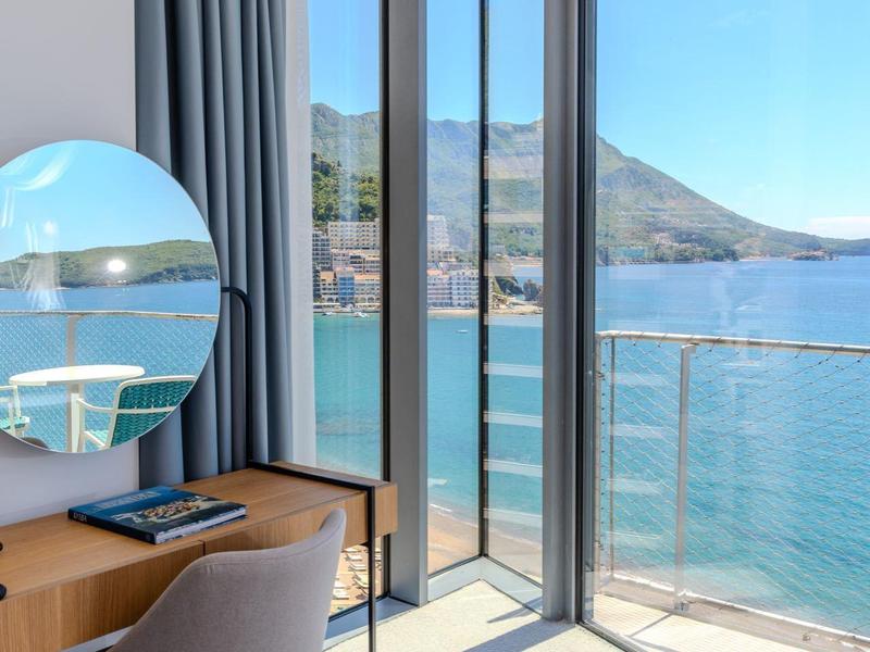 Helles Zimmer mit großem Fenster, blauem Vorhang, Schreibtisch und Meerblick.