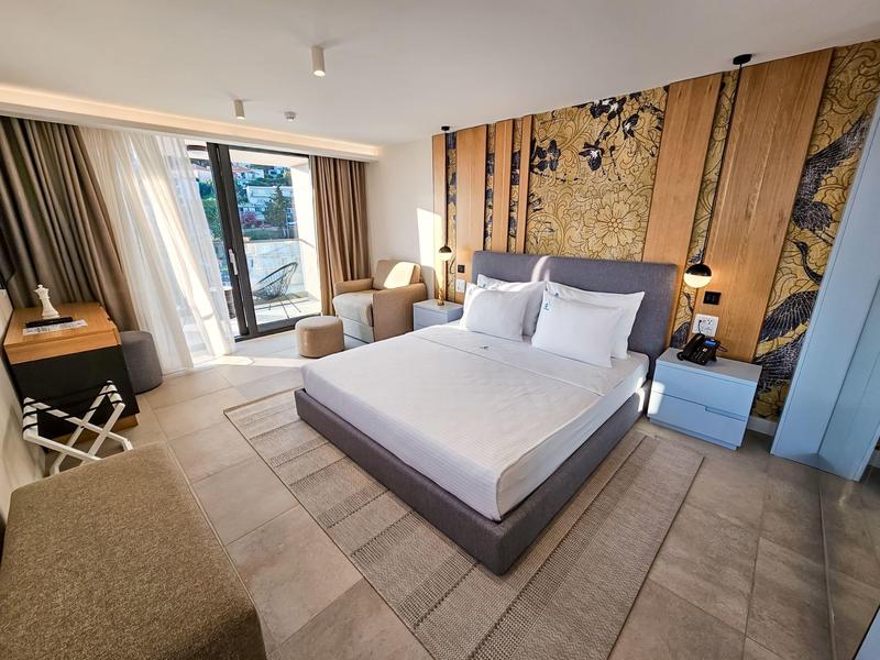 Nowoczesny pokój hotelowy z podwójnym łóżkiem, fotelami i balkonem z widokiem na zewnątrz.