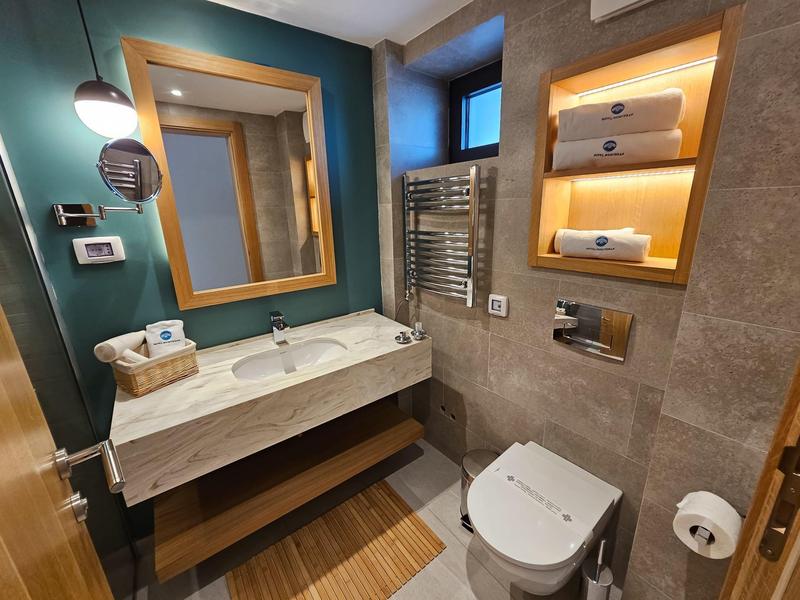 Kompaktowa łazienka hotelowa z umywalką, podświetlanym lustrem, toaletą i grzejnikiem na ręczniki.