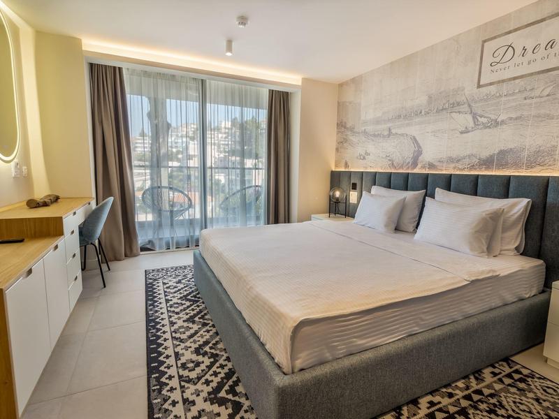 Nowoczesny pokój hotelowy z dużym łóżkiem podwójnym, biurkiem i balkonem z widokiem na miasto.