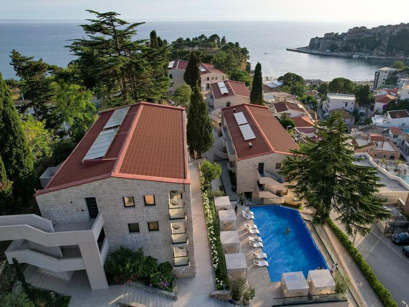 Widok na hotel z basenem, czerwonymi dachami i morzem w tle na wybrzeżu.
