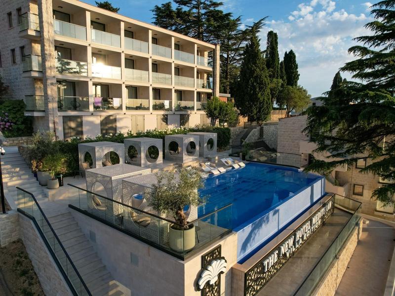 Hotel z basenem na tarasie, otoczony drzewami i budynkami w słoneczną pogodę.