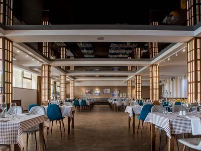 Großer, eleganter Speisesaal mit weißen Tischdecken und blauen Sesseln in einem Hotel.