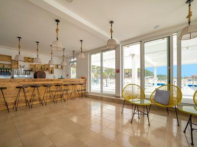 Helles Café mit Holztheke, Hockern und großen Fenstern mit Blick auf das Meer.