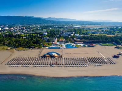 Pláž s řadami lehátek a slunečníků před přímořským městem a horami v pozadí