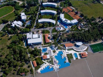 Luftaufnahme eines Hotels mit Poolbereich, umgeben von grünen Feldern und Sportplätzen.
