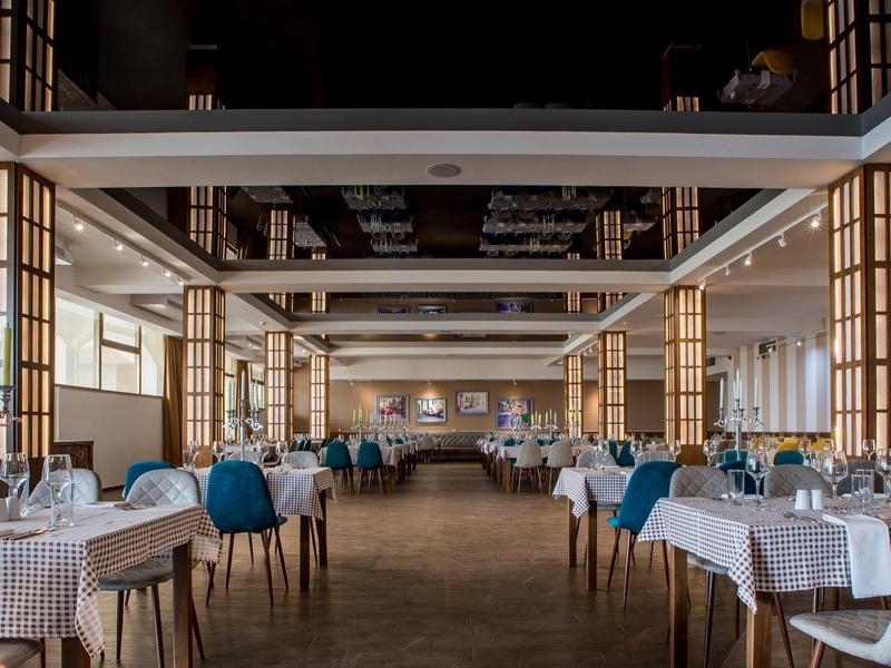 Elegantní restaurace s bílými prostřenými stoly a modrými židlemi v světlém prostoru.