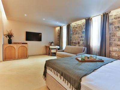 Helles Hotelzimmer mit Steinwand, Doppelbett, Sofa, TV und Schreibtisch unter Fenster mit Vorhängen.