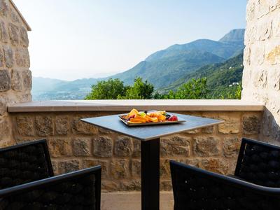Balkon mit schwarzem Tisch, zwei Stühlen, Steiwand und Berglandschaft im Hintergrund bei klarem Himmel.
