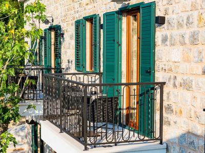 Hausfassade aus grobem Stein mit grünen Fensterläden und Balkon mit schwarzem Eisengeländer.