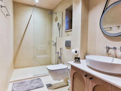 Schlankes Badezimmer mit beiger Wand, Glasdusche, Wandtoilette, rundem Spiegel und weißem Waschbecken.