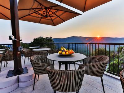 Terrasse mit runden Tischen, Stühlen und Sonnenschirmen bei Sonnenuntergang in den Bergen.