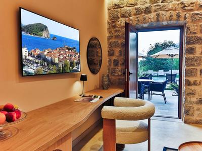 Heller Raum mit Holzmöbeln, Fernseher an der Wand, Barhocker und Blick auf Terrasse mit Sonnenschirm.