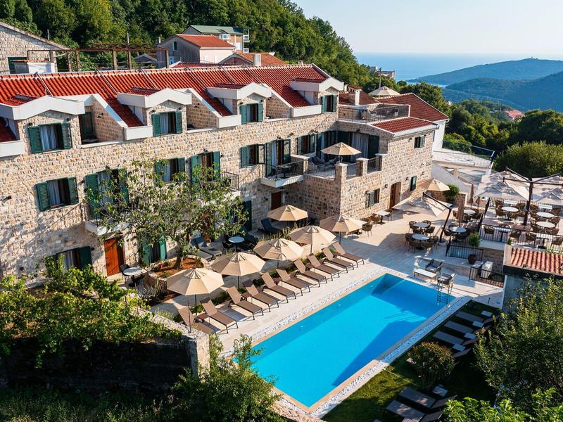 Großes Steinhaus mit rotem Ziegeldach, Terrasse mit Sonnenschirmen und blauem Swimmingpool.