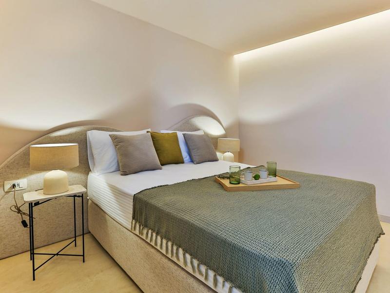 Modernes Schlafzimmer mit großem Bett, grauer Decke, Nachttischlampen und weicher Beleuchtung.