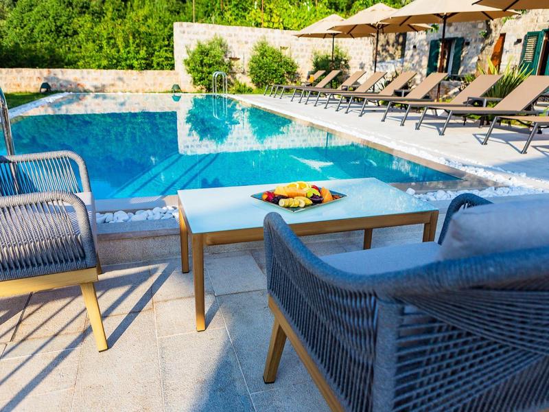 Moderner Pool mit blauer Wasserfläche, Sonnenliegen, Schirmen und Gartenmöbeln im Freien.