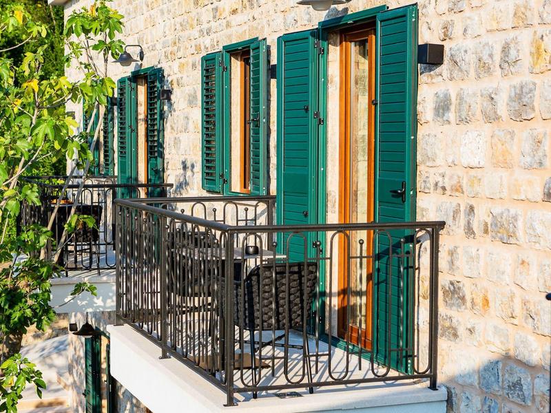 Hausfassade aus grobem Stein mit grünen Fensterläden und Balkon mit schwarzem Eisengeländer.