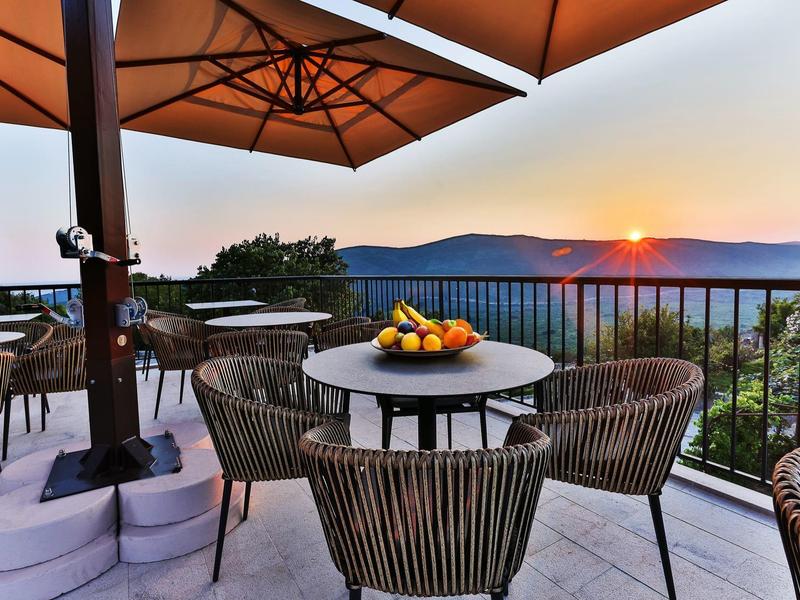 Terrasse mit runden Tischen, Stühlen und Sonnenschirmen bei Sonnenuntergang in den Bergen.