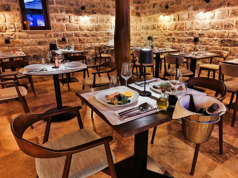 Gemütliches Restaurant mit Holztischen, Weinflaschen und warmem Steinhaus-Ambiente bei Abendlicht.