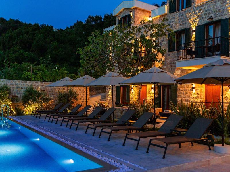 Abendlicher Poolbereich mit Liegestühlen und Sonnenschirmen vor einem beleuchteten Steinhaus.